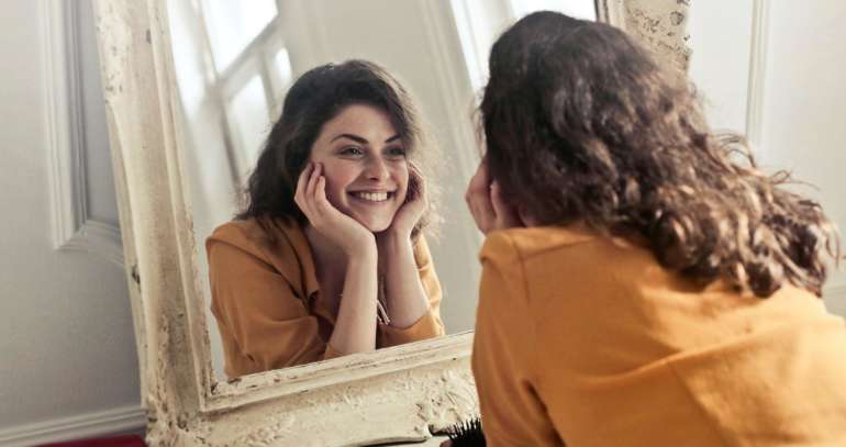Nainen katsoo peiliin ja hymyilee peilikuvalleen.